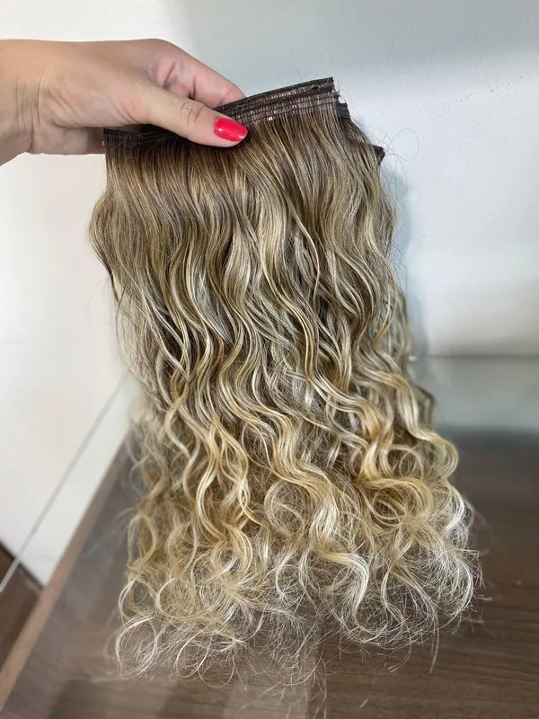 Mão segurando duas telas de cabelo ondulado com a faixa de fita no topo